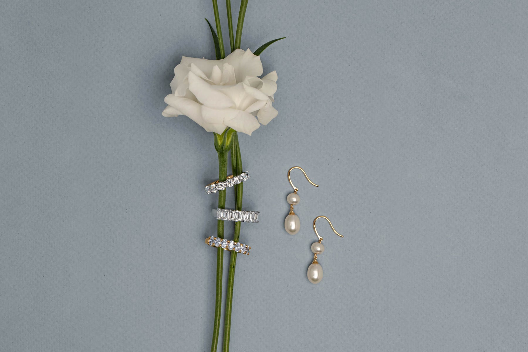 Diamond Bands on white rose stem with Yellow Gold Rosie Pearl Earrings next to them