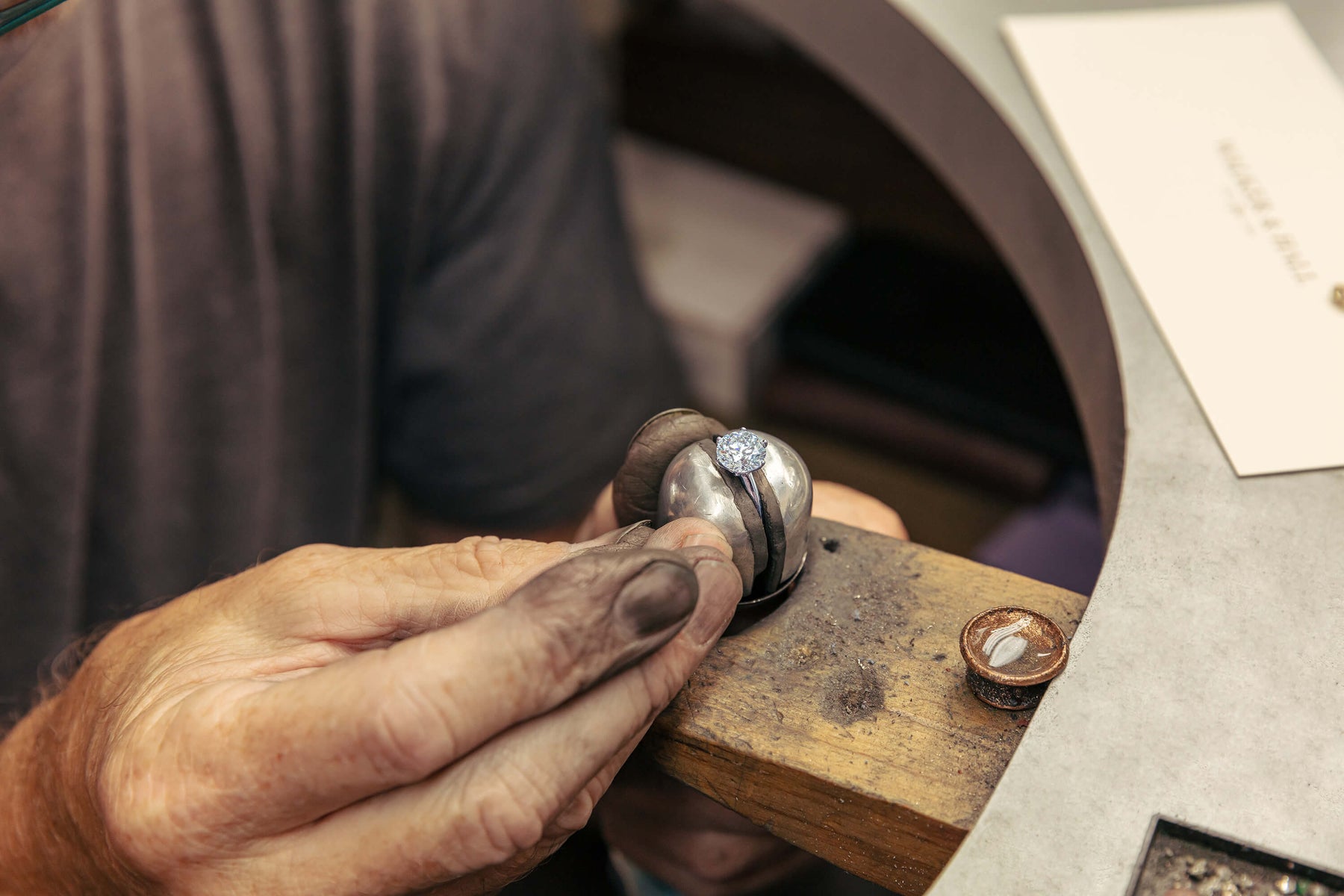 Close-up of a jeweller's hands at jewellery bench working on a diamond solitaire ring with a focus on the hands and tool.