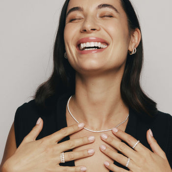 Woman smiling wearing Panorama diamond tennis necklace, diamond earrings and rings