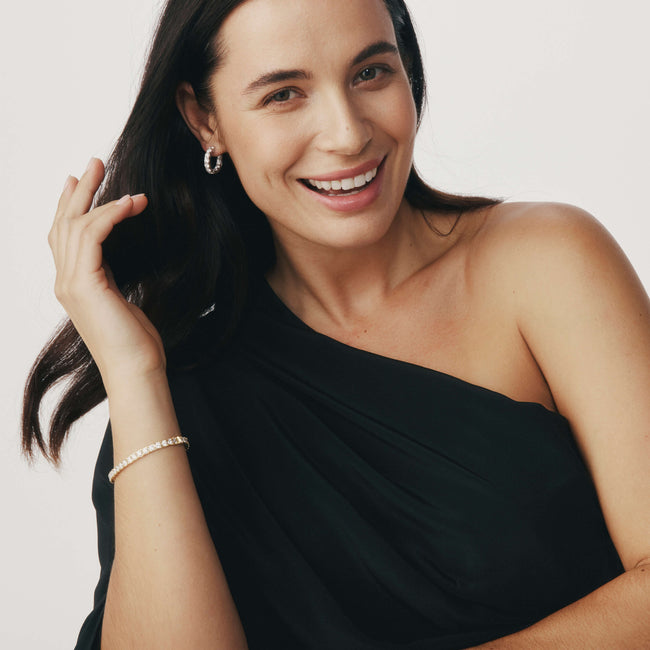 Woman smiling wearing diamond Jubilee Earrings and Bracelet and a black one-shoulder dress.