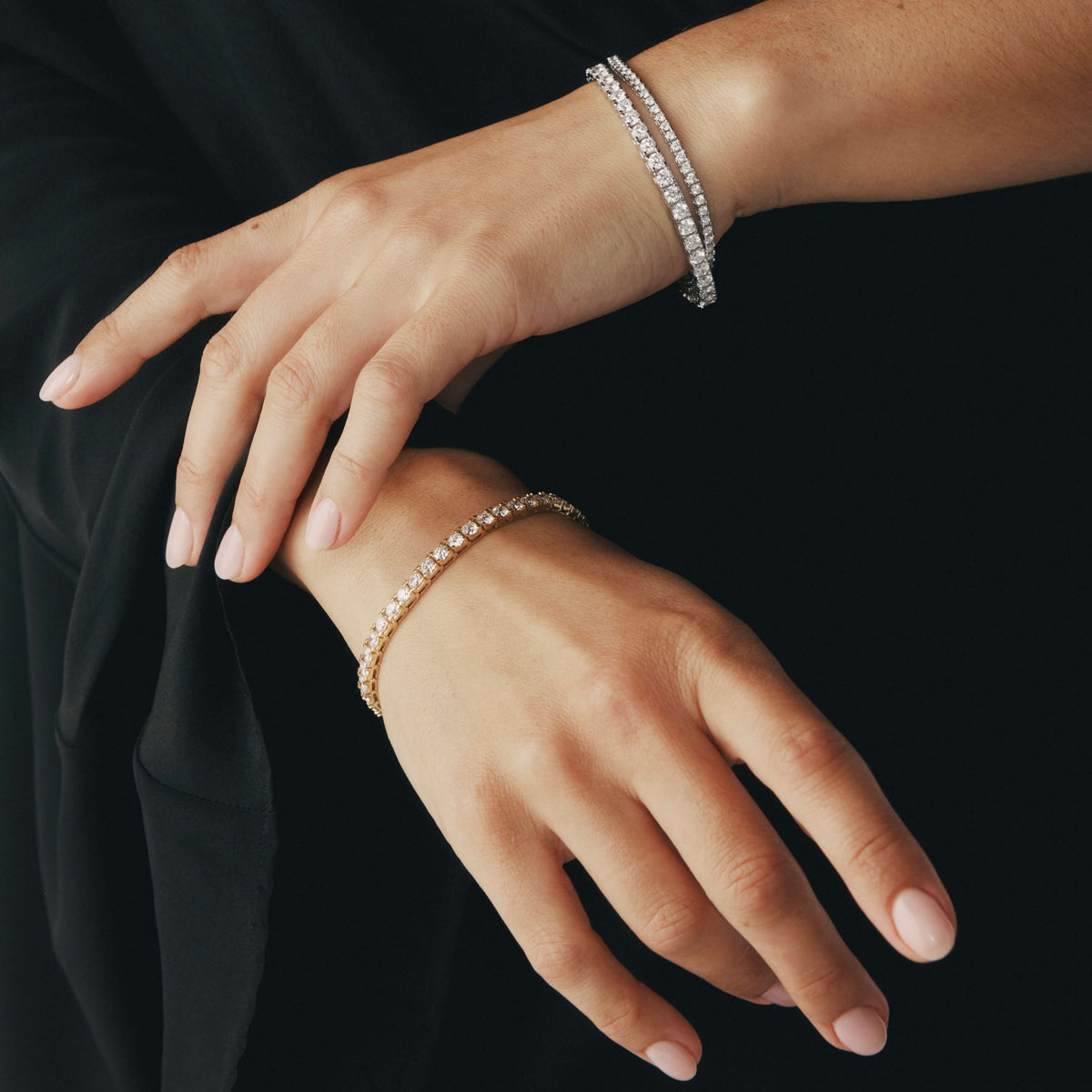 Close-up of hands wearing diamond bracelets on a black background