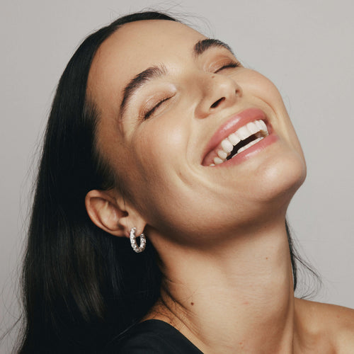 Woman with a radiant smile wearing Diamond Jubilee Hoop Earrings against a neutral background