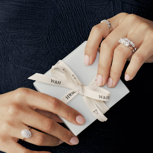 Close up of model holding wrapped Walker & Hall gift box wearing diamond rings