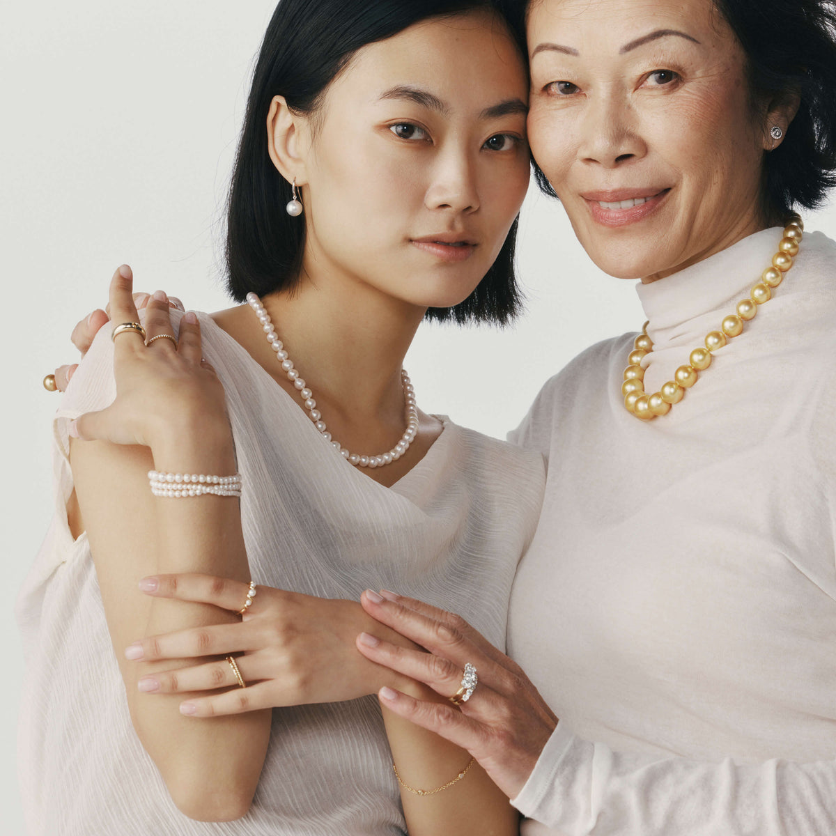 Mother and daughter with their arms around one another wearing pearl jewellery