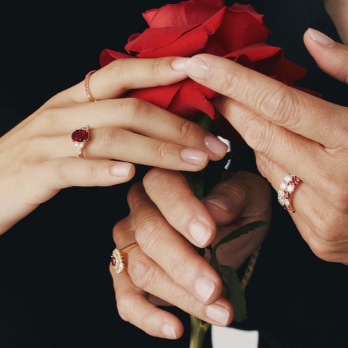Close up of hands holding a red rose wearing ruby and diamond rings