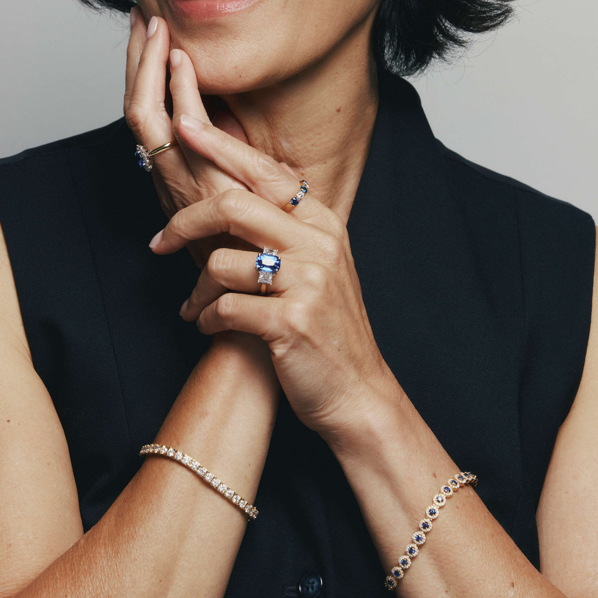 Close up of model's hands wearing sapphire and diamond rings and bracelets