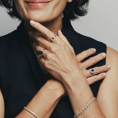 Close-up of a person wearing multiple sapphire and diamond rings and a sapphire and diamond bracelet against a neutral background