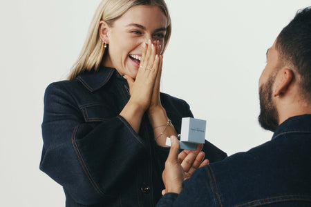 Man on one knee proposing to his partner with an open Walker & Hall ring box