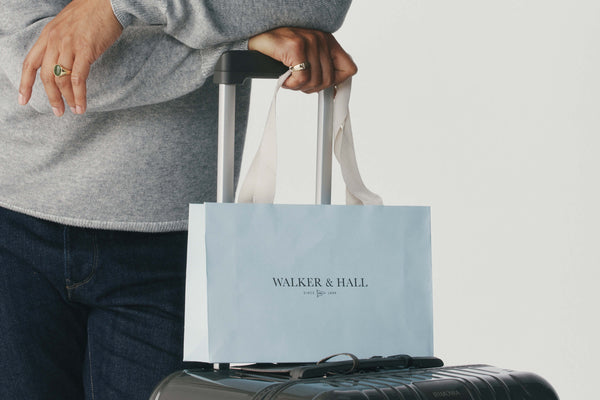 Person holding a suitcase with a Walker & Hall shopping bag on a light gray background