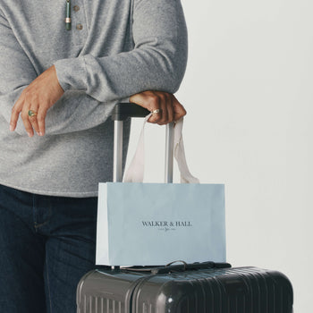 Person holding a Walker & Hall gift bag and the handle of a suitcase