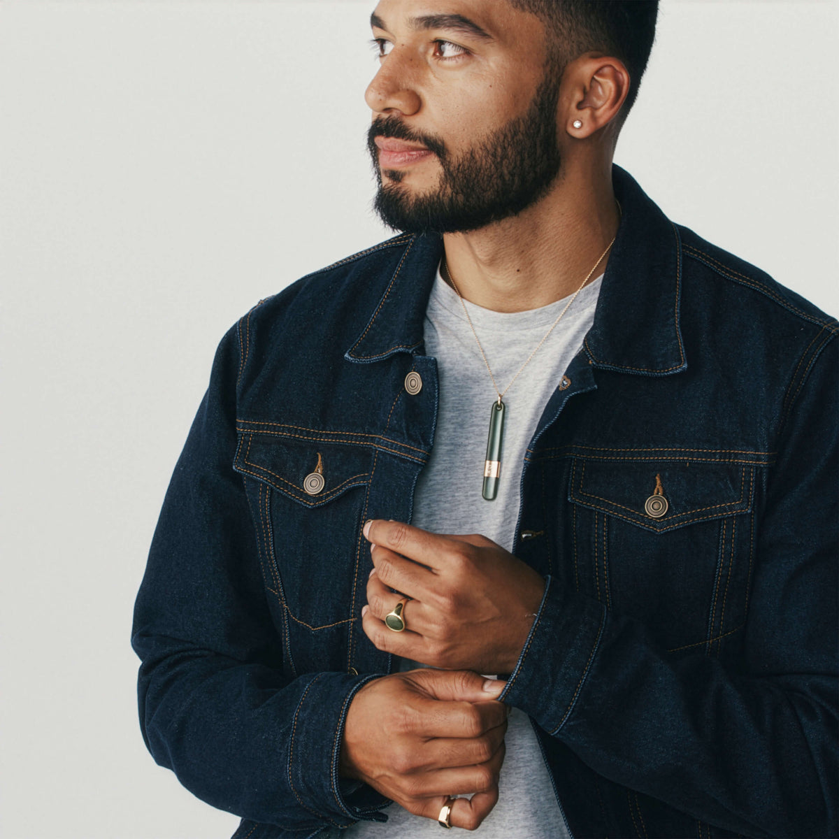Male model wearing denim jacket and gold and greenstone rings and pendant