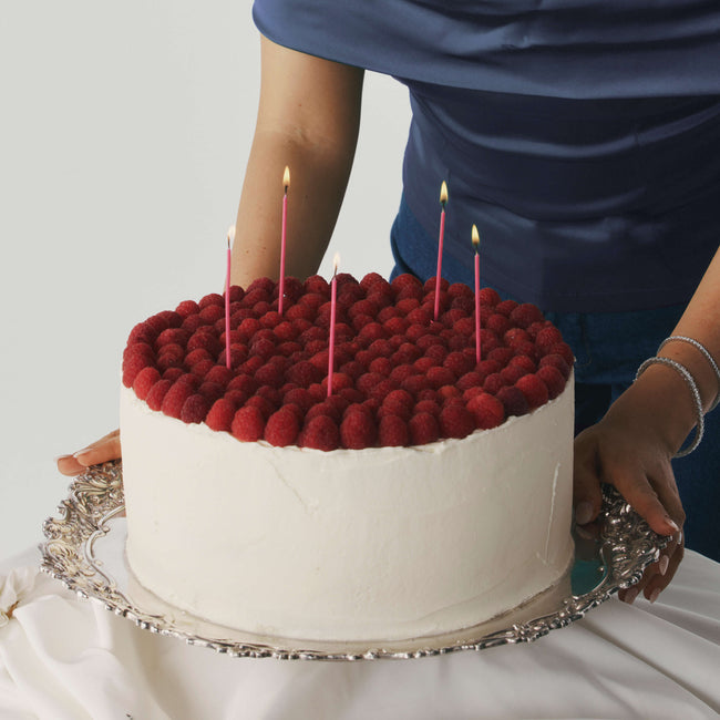 Cake with red berry decoration and lit candles on a white background